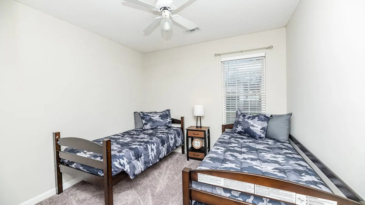 A relaxed bedroom with two beds, each with simple bedding, and a nightstand between them. A window lets in natural light, creating an inviting space well-suited for families or friends.