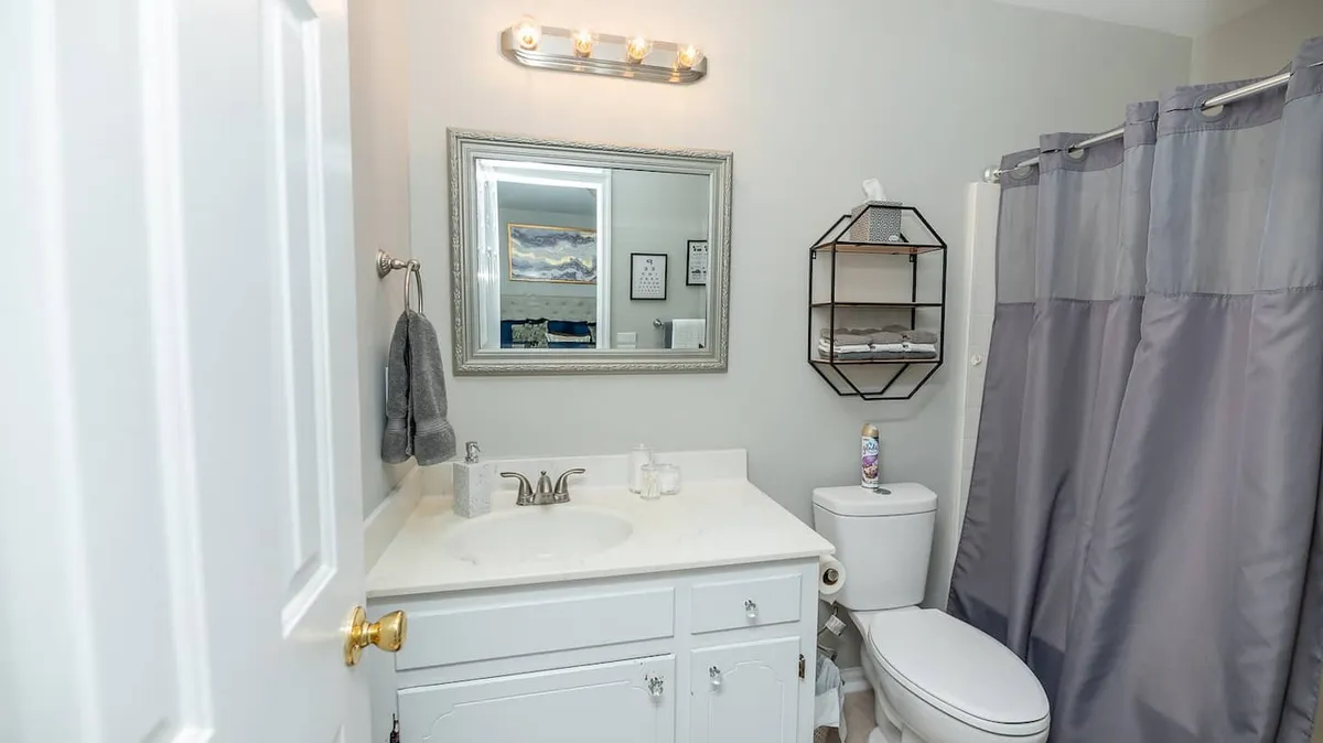 A fresh, inviting bathroom scene featuring a sink, mirror, shower curtain, toilet, and tasteful wall decor. The space is bright and clean, designed for both relaxation and practicality.