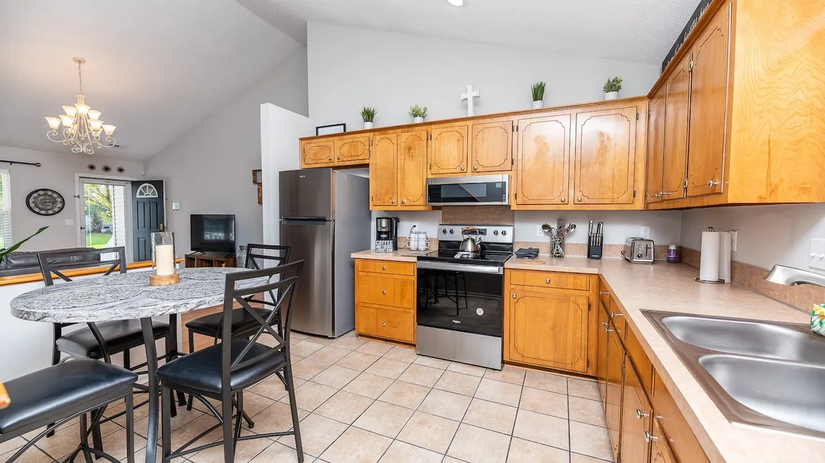 A cozy kitchen and dining area with a kitchen island, stainless steel appliances, wooden cabinets, and a dining table set up for family meals. The space feels homey and perfect for group gatherings.