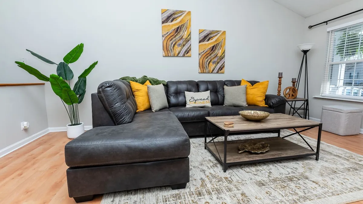 A stylish living area featuring a leather sectional sofa topped with decorative pillows, a sleek coffee table, abstract wall art, and an indoor plant. The space is both comfortable and visually appealing, inviting guests to sit back and enjoy quiet moments or lively conversation.