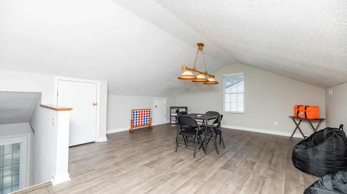 This interior image features a dining table surrounded by a bean bag chair, a colorful game board set up for play, and stylish light fixtures. The playful, relaxed mood and focus on game-night activities are evident, evoking a fun and welcoming family gathering space.