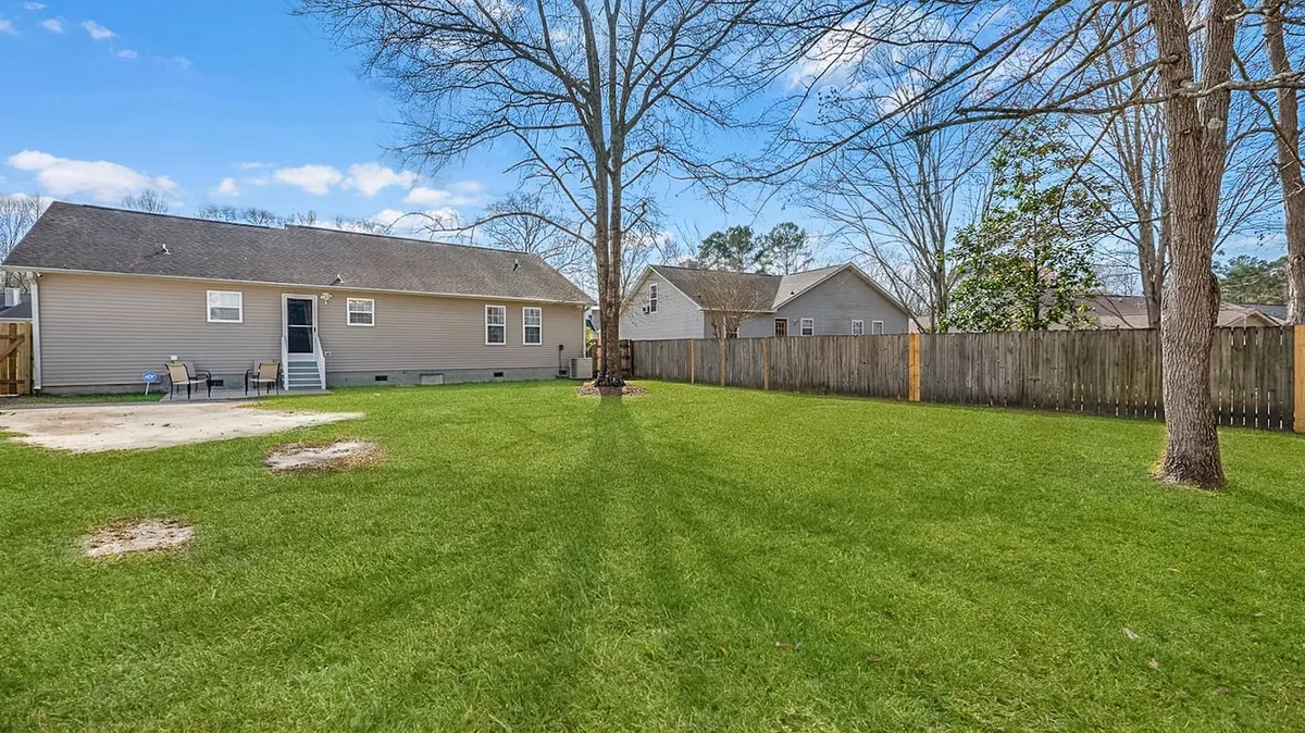 A spacious backyard featuring a large tree, open green space, and the rear view of the house—an inviting area where families can gather, children can play, and pets can roam. The space feels private and safe for outdoor activities.