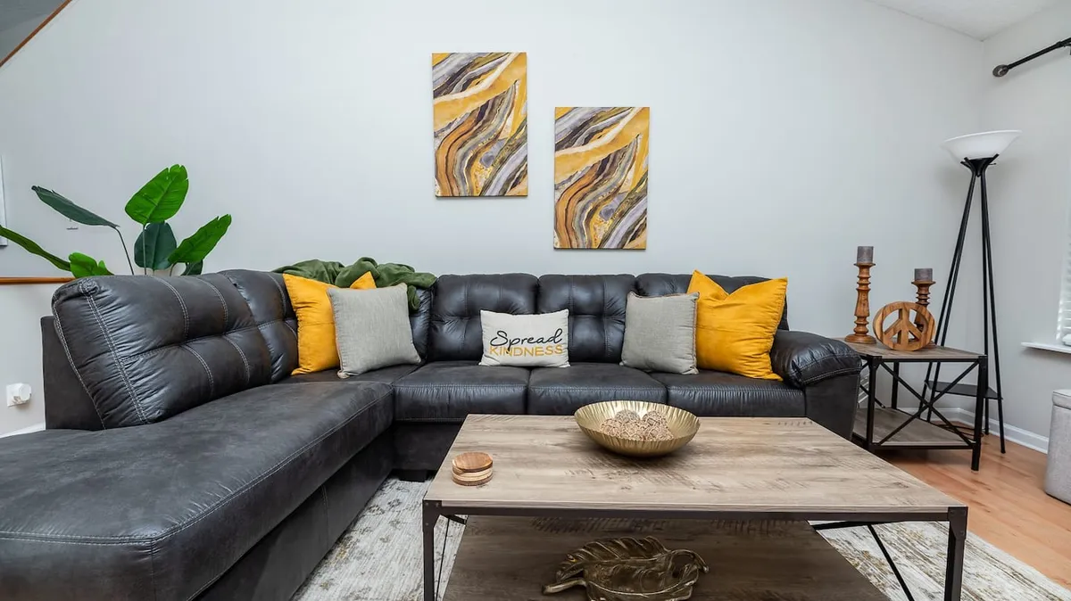 A warm and welcoming living room featuring a cozy sofa, artistic decor, and a coffee table designed for gathering. The arrangement invites casual conversation, board games, or simply relaxing together after a day out exploring Charleston.