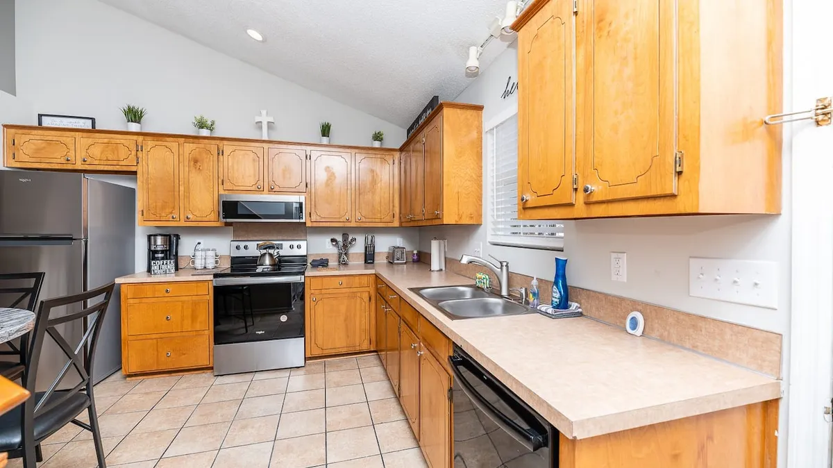 A spacious and inviting kitchen featuring wood cabinetry, modern stainless steel appliances, a central kitchen island, and a sink with a window view. There is ample counter space for meal preparation and the overall design promotes ease of use.