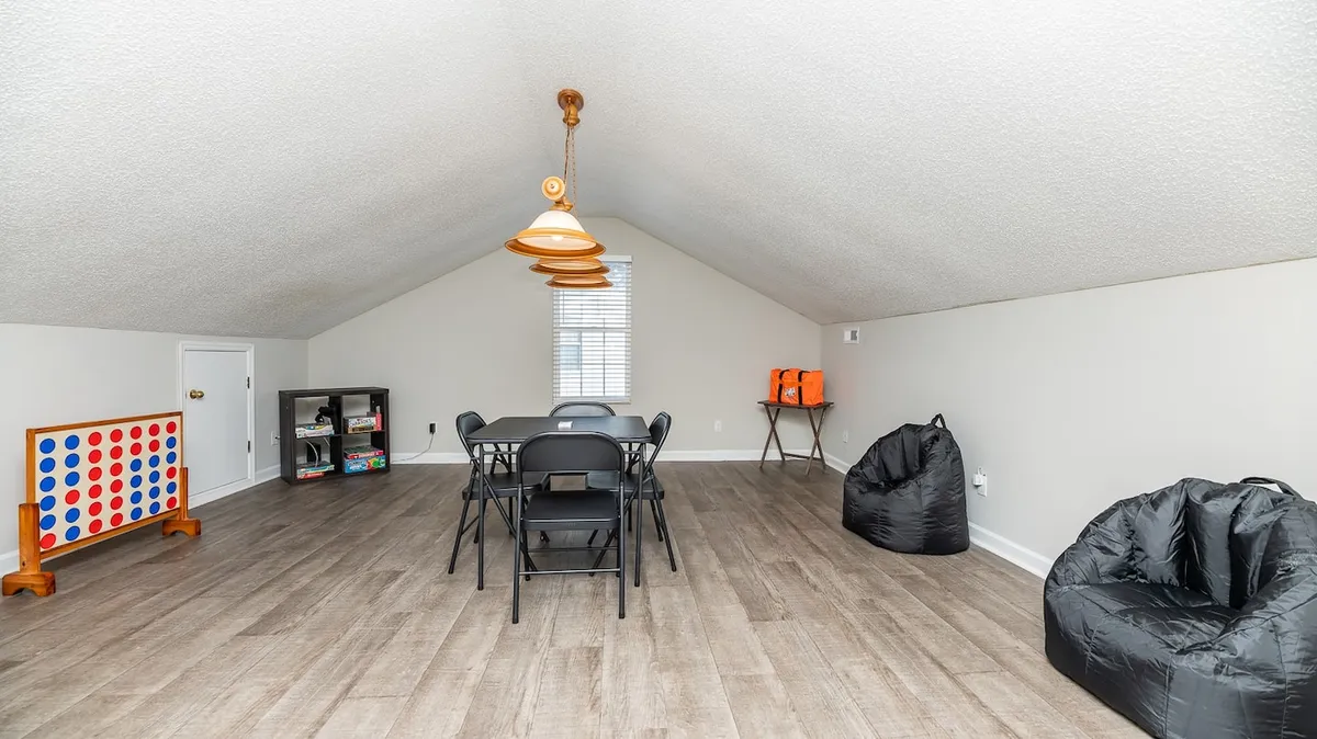 A lively dining area set with a large table surrounded by chairs, playful bean bag seats, a giant Connect Four game, and stylish suspended lighting. The setup encourages both dining and recreational activities for groups or families.